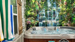 A hot tub with a waterfall backdrop, a towel rack, and a safety sign. - NEW CABIN ~HOT TUB IN THEATER~1 QUIET ACRE ~HIKING ~FIRE PIT ~KING SUITES (Columbia)