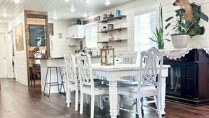 A dining area with a wooden floor, white dining table, and chairs, a kitchen area with cabinets and a plant, and a deer head decoration on the wall. - NEW CABIN ~HOT TUB IN THEATER~1 QUIET ACRE ~HIKING ~FIRE PIT ~KING SUITES (Columbia)
