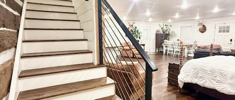 Un escalier avec des marches en bois et une rampe en métal menant à une pièce où se trouvent un lit et une table.