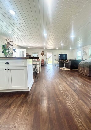A spacious living area with a wooden floor, white cabinetry, and a television. - NEW CABIN ~HOT TUB IN THEATER~1 QUIET ACRE ~HIKING ~FIRE PIT ~KING SUITES (Columbia)