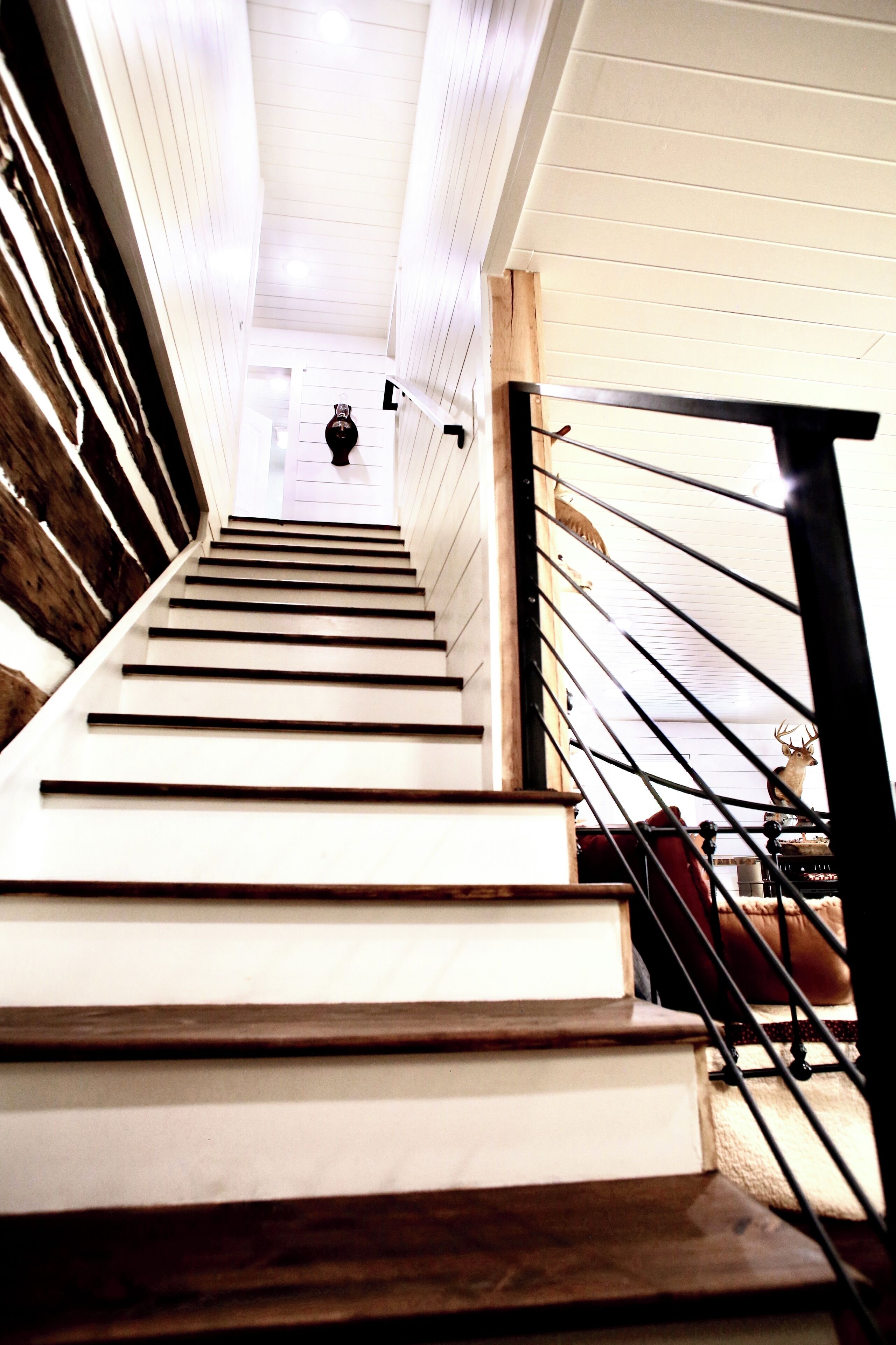 Una escalera con peldaños blancos y barandilla negra, que conduce a una habitación con techo blanco y un pequeño adorno en la pared.