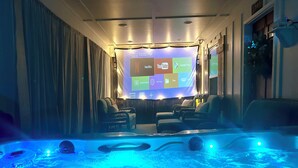A room with a large screen displaying streaming services, a heated floor, and a seating area with sofas. - NEW CABIN ~HOT TUB IN THEATER~1 QUIET ACRE ~HIKING ~FIRE PIT ~KING SUITES (Columbia)