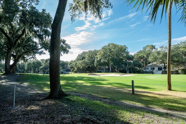 A golf course with a clear path, trees, and a distant building.