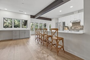 A modern kitchen with white cabinets, a central island, and a dining area with wooden chairs. - Fabulous 5 BR/3.5 BA on 17th Fairway! Screen Porch! Amenity access included (Seabrook Island)