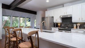 A modern kitchen with white cabinetry, stainless steel appliances, and a large island with bar stools.