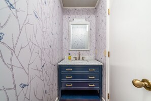 A bathroom with a marble sink, a mirror, and a blue vanity with gold handles.