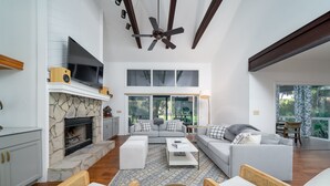 A modern living room with a stone fireplace, grey sofas, and a ceiling fan.