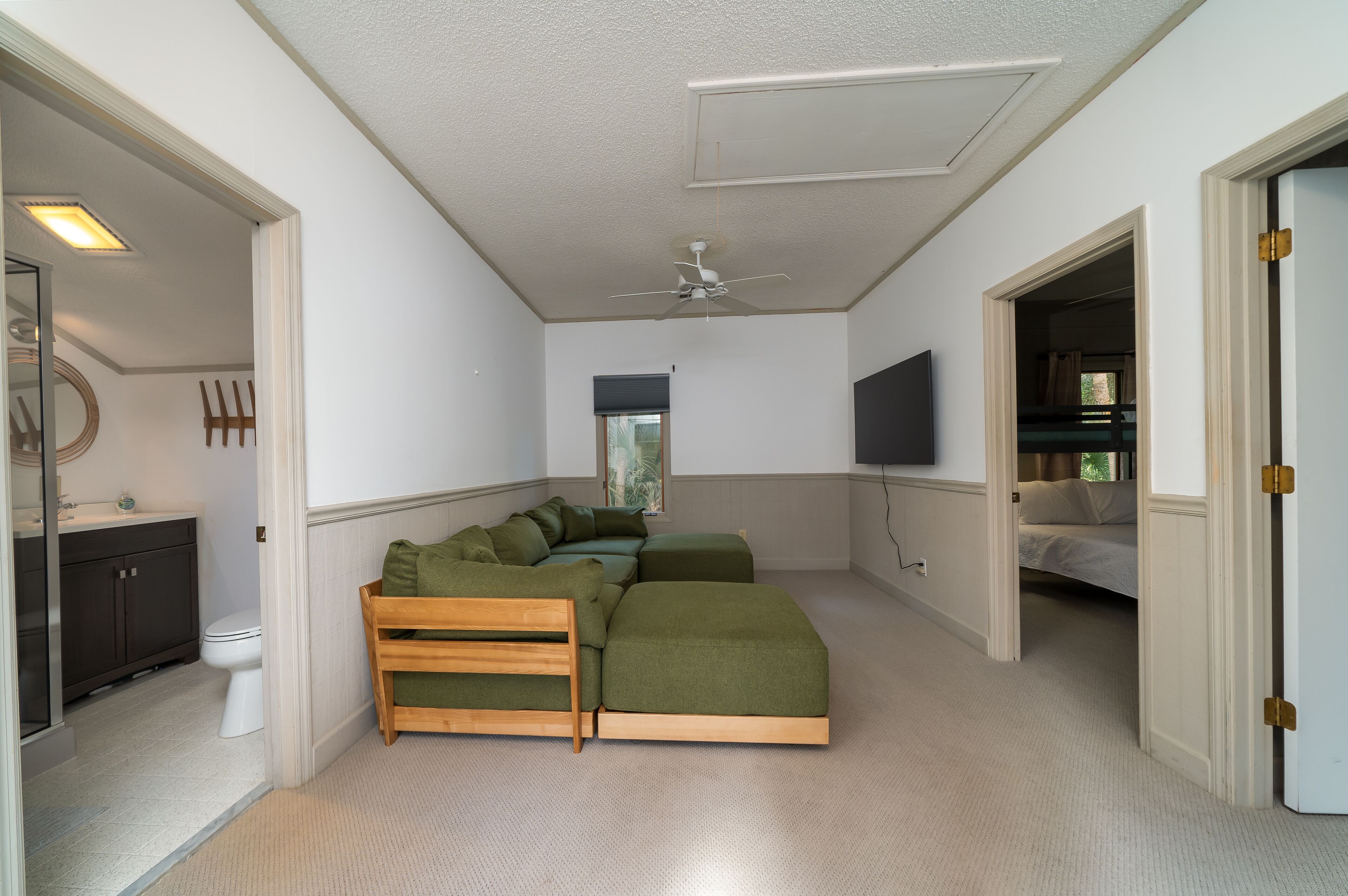 A bedroom with a large bed, a ceiling fan, a TV, and a bathroom with a toilet and sink.