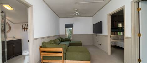 A bedroom with a large bed, a ceiling fan, a TV, and a bathroom with a toilet and sink.