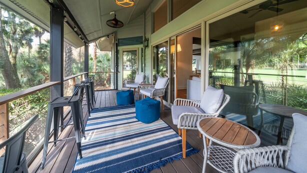 A covered outdoor seating area with wicker furniture, a blue and white striped rug, and a ceiling fan.