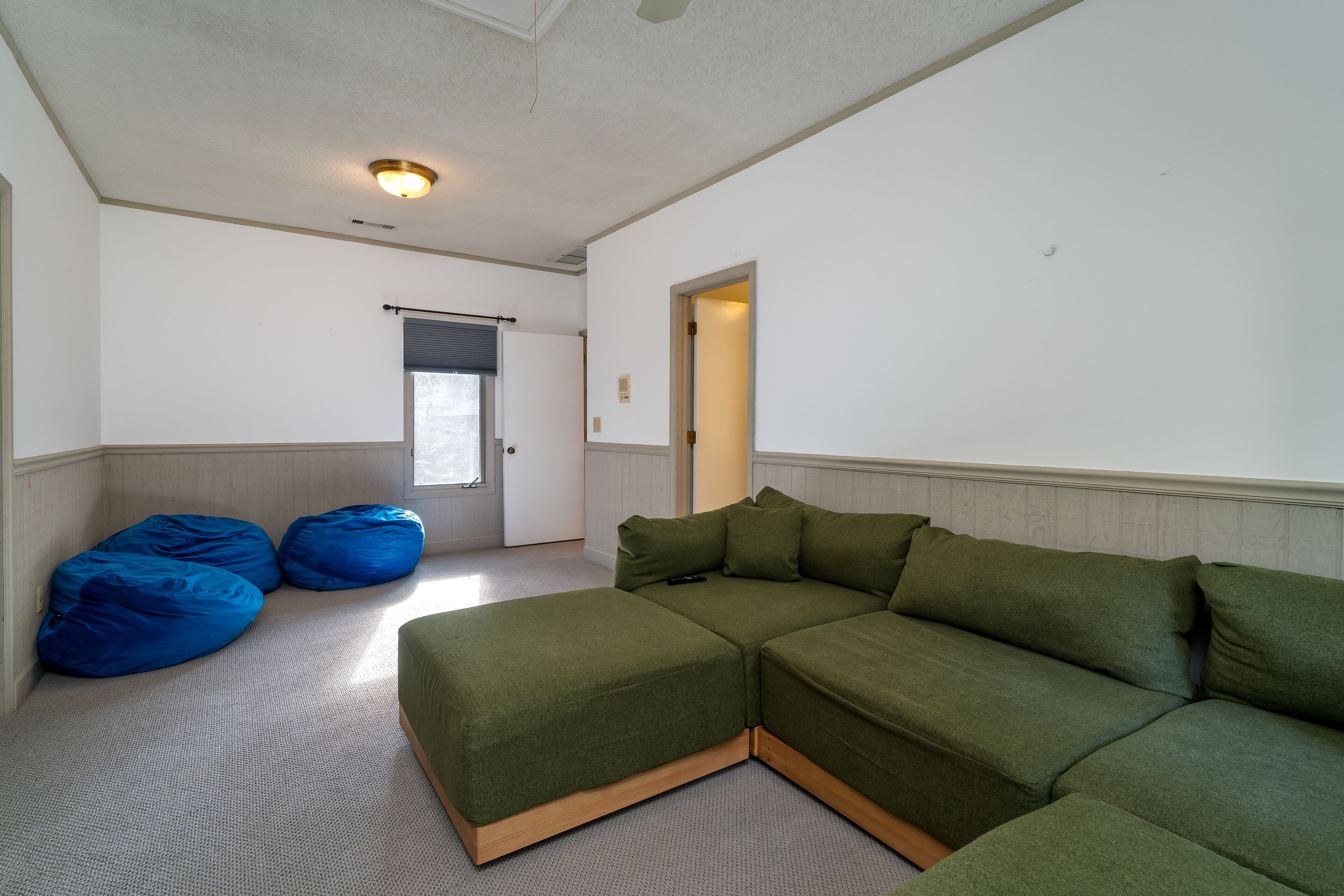 Una sala de estar con un sofá modular, dos pufs y una puerta que da a otra habitación.