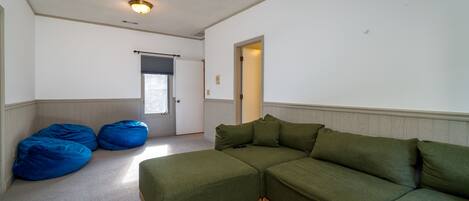 Una sala de estar con un sofá modular, dos pufs y una puerta que da a otra habitación.