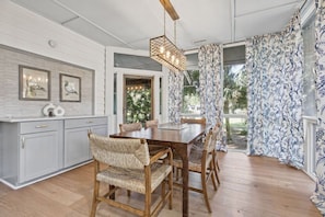 A dining area with a wooden table and woven chairs, a hanging light fixture, and a view of greenery outside. - Fabulous 5 BR/3.5 BA on 17th Fairway! Screen Porch! Amenity access included (Seabrook Island)
