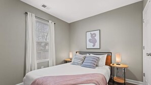 A bedroom with a bed, bedside tables, a window with curtains, a wall-mounted artwork, and a door. - Sleeps 8. Cozy Bungalow in Downtown Georgetown (Georgetown)