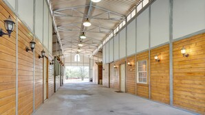 A long, narrow indoor space with wooden walls and a concrete floor, featuring multiple doors and wall-mounted lights. - Georgetown Barn Studio on > 7 Acres: Pet Friendly! (Georgetown)