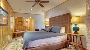 A bedroom with a large bed, wooden walls, a ceiling fan, and a stone accent wall. - Georgetown Barn Studio on > 7 Acres: Pet Friendly! (Georgetown)