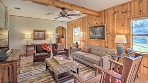 A cozy living room with wooden paneling, a ceiling fan, a fireplace, and a large window. - Georgetown Barn Studio on > 7 Acres: Pet Friendly! (Georgetown)