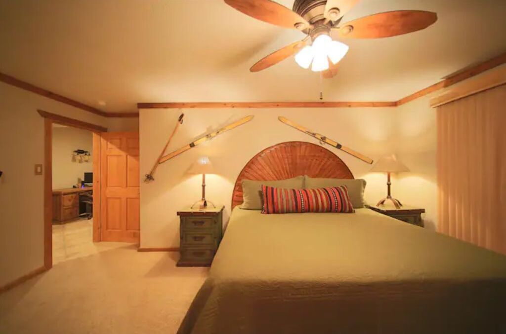Une chambre à coucher avec un lit, deux tables de chevet, un ventilateur de plafond et une tête de lit en bois.