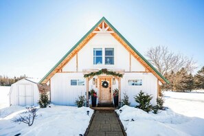 A white house with a green roof, a front porch, and a wreath on the door.