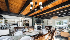 Una cocina moderna con vigas de madera, un comedor con una mesa grande dispuesta para seis personas y un espacio de sala acogedor con chimenea.