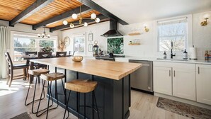 Una cocina moderna con una isla de madera, taburetes de bar, un ventanal grande y una campana extractora negra.