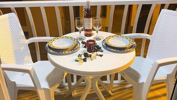 A round table with two white plastic chairs, a bottle of wine, two wine glasses, and a plate with food remnants. - Charming and Chic - Kaylan Seaside Apartment 2 (St. Paul's Bay)