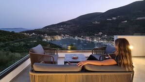 A balcony with wicker furniture overlooking a marina and a town. - Villa Roya in Sivota (Lefkada)