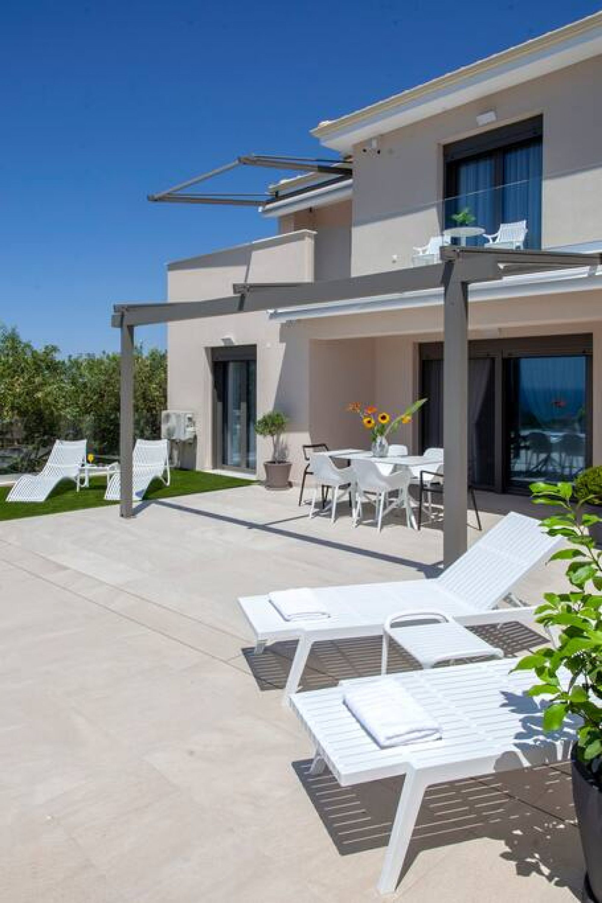 A modern house with a patio area featuring white lounge chairs and a dining table.