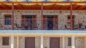 A two-story building with a balcony, stone walls, and wooden doors. - Agios Petros Apartments 1 (Lefkada)