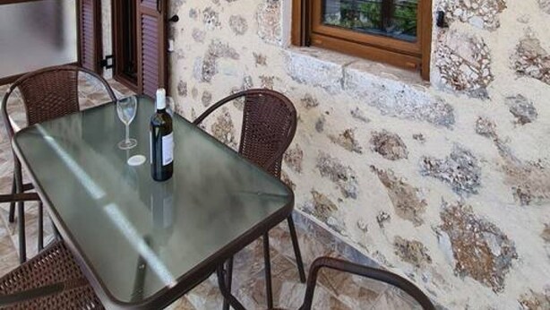 A dining area with a table and chairs, a bottle of wine, and a window with a view. - Agios Petros Apartments 1 (Lefkada)
