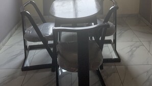 Een kamer met een ronde tafel en vier stoelen, een raam met uitzicht op een verafgelegen landschap en een betegelde vloer.