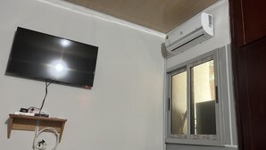 Een kamer met een wandtelevisie, een airconditioningapparaat en een raam met uitzicht.