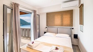 A hotel room with a bed, a view of the sea, and a balcony with curtains. - Villa Irene 1 Drakatos (Lefkada)