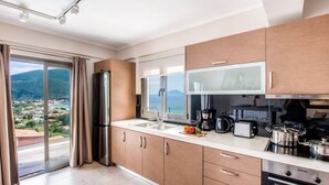 A modern kitchen with a large window, a built-in oven, and a coffee maker. - Villa Irene 1 Drakatos (Lefkada)