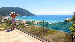 A person taking a photo of a coastal view from a balcony with a wooden floor and glass railing. - Villa Irene 1 Drakatos (Lefkada)