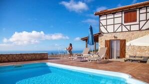 Une piscine avec des chaises longues et un bâtiment en pierre doté d’un toit en tuiles.