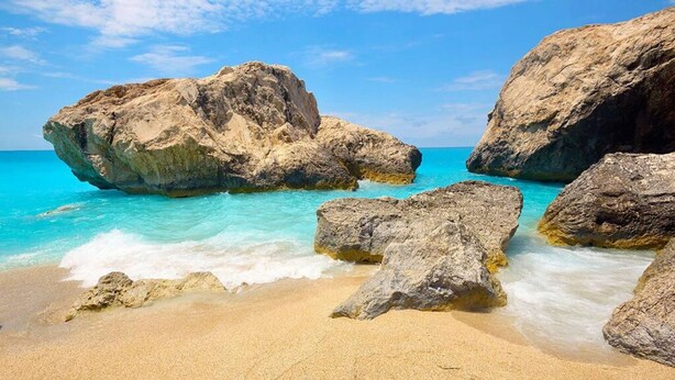 Une plage avec de gros rochers et une eau turquoise cristalline.