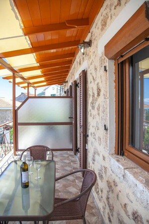 A covered outdoor seating area with a table and chairs, a bottle of wine, and a view of the surrounding landscape. - Agios Petros Apartments 2 (Lefkada)