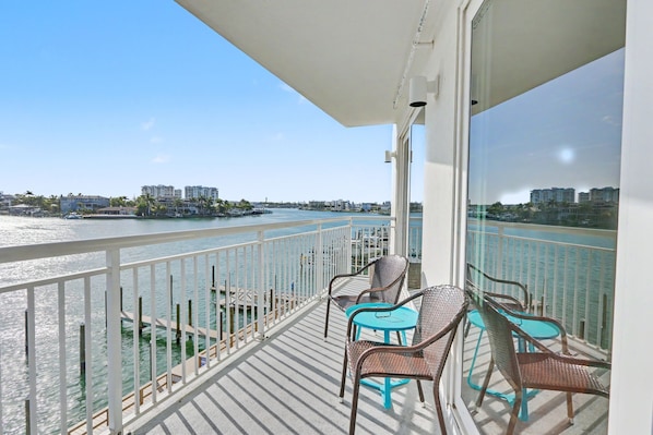 Un balcon donnant sur une rivière, avec des balustrades blanches et des meubles en osier.
