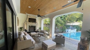 A spacious patio with a fireplace, outdoor seating, and a pool view.