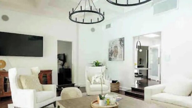 A modern living room with a large flat-screen TV, white sofas, a wooden coffee table, and a chandelier.