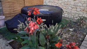 Un jacuzzi en un jardín con plantas y un muro de piedra al fondo.