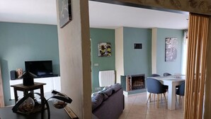 Una sala de estar con sofá, una mesa de comedor con sillas, chimenea y televisor.
