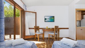 Una habitación con dos camas, una mesa de comedor con sillas, un cuadro en la pared y vistas a la vegetación exterior.