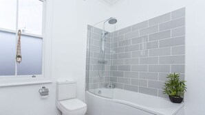 Un baño moderno con inodoro, ducha con cabina de vidrio y una planta en maceta.