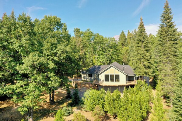 A house surrounded by dense forest, with a large deck and multiple windows. - Winterfell Estates, Luxury home in Mt. Shasta. (Mount Shasta)