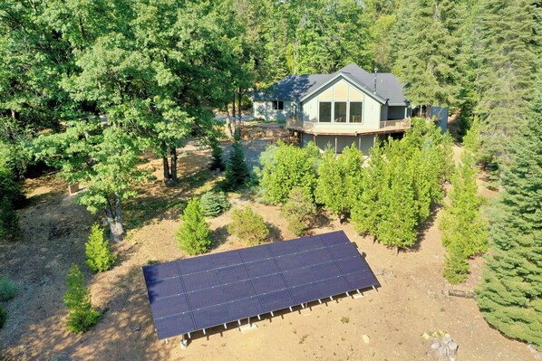 A house surrounded by dense trees, with a solar panel array in the foreground.
