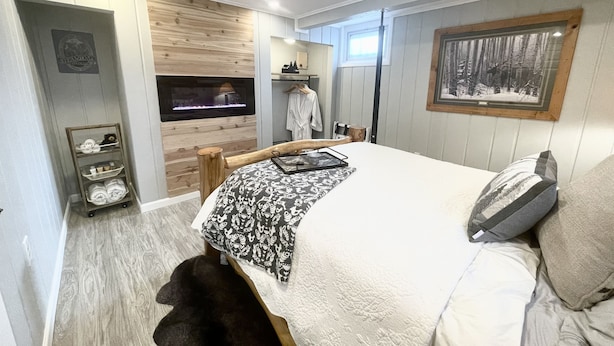 Une chambre moderne avec un grand lit, une cheminée, un mur en bois et un tableau encadré.