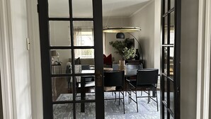 An open door leading to a dining area with a table and chairs, a rug, and a hanging light fixture.