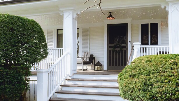 A white two-story house with a porch, steps, and a small table with chairs.